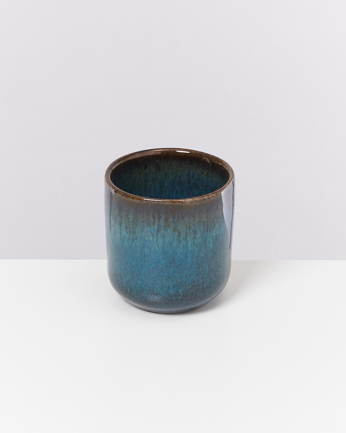 Keramikbecher mit blau-brauner Glasur auf weißem Hintergrund.