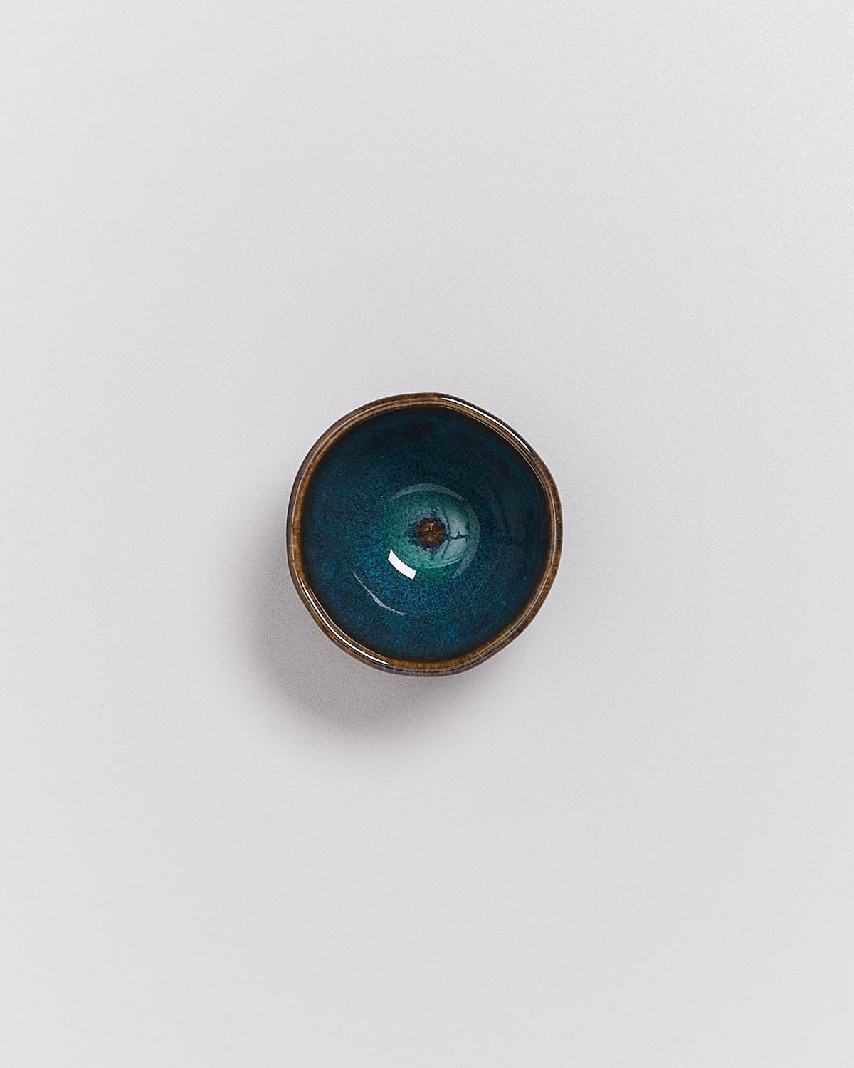 Kleine, runde Schale mit blau-grüner Glasur und braunem Rand auf weißem Hintergrund.