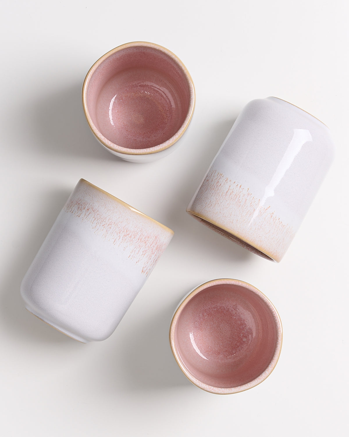 Vier Keramikbecher mit rosa Innenfläche und weißer Außenseite liegen auf einem weißen Untergrund.