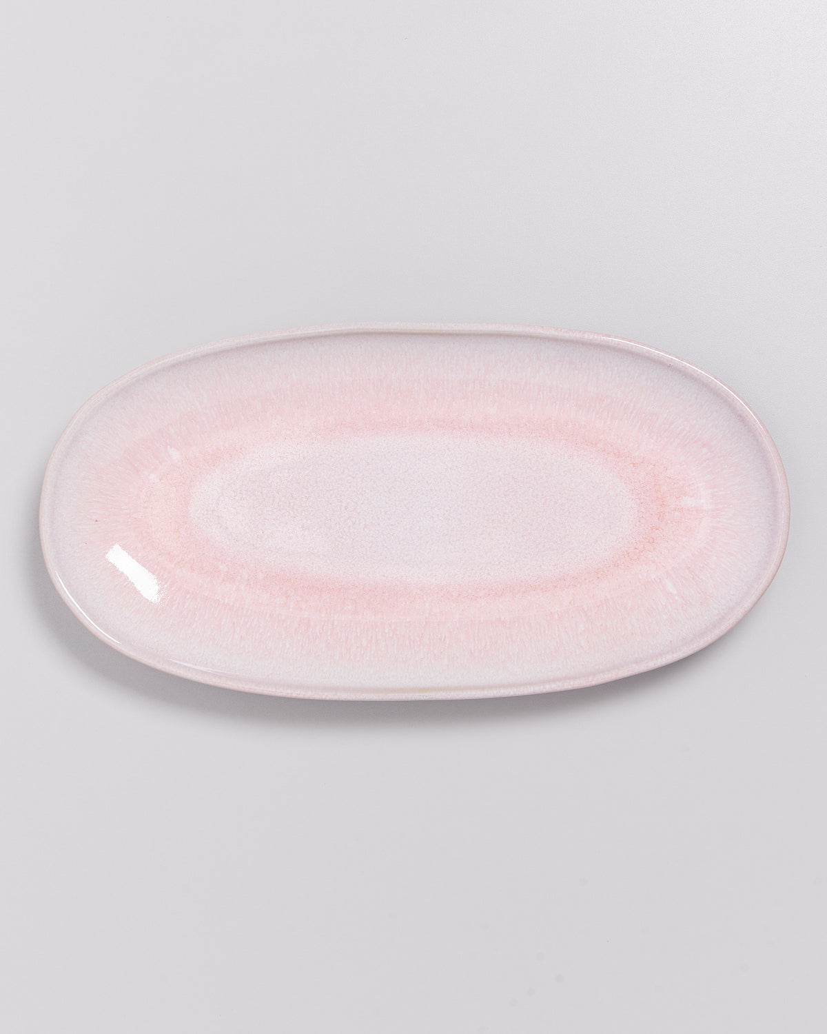 Ein ovaler Teller in zartem Rosa mit glatter Oberfläche auf einem weißen Hintergrund.