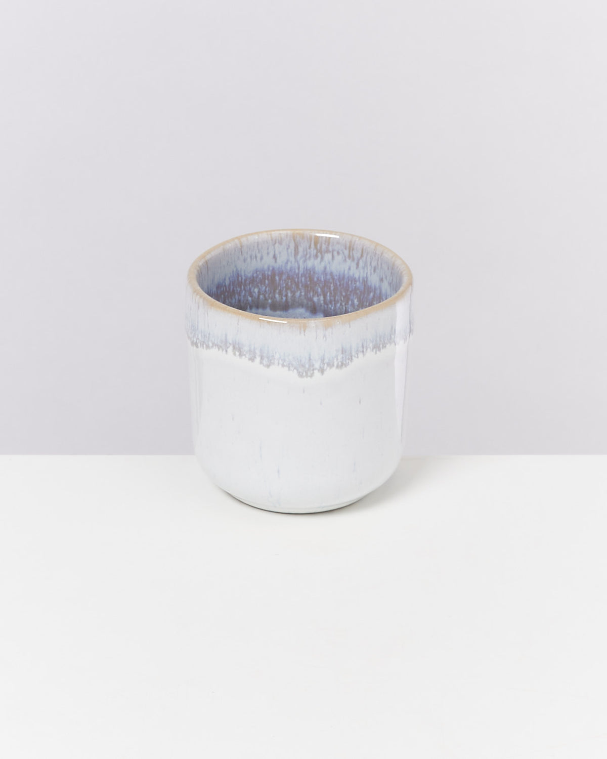 Keramikbecher mit blau-weißer Glasur auf einem weißen Tisch vor einem grauen Hintergrund.