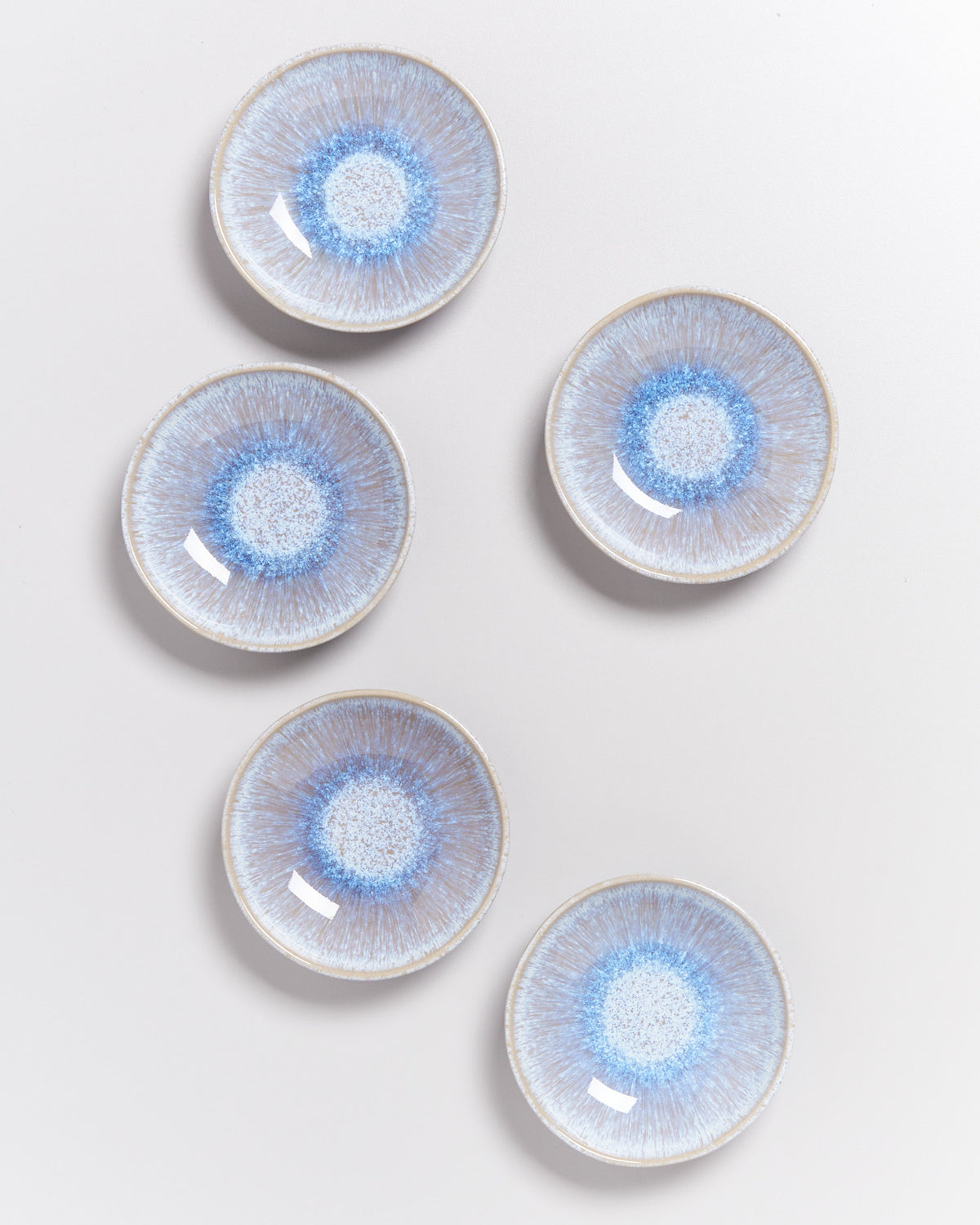 Fünf runde Keramikteller in creme und blau, gleichmäßig auf einer hellen Oberfläche angeordnet.