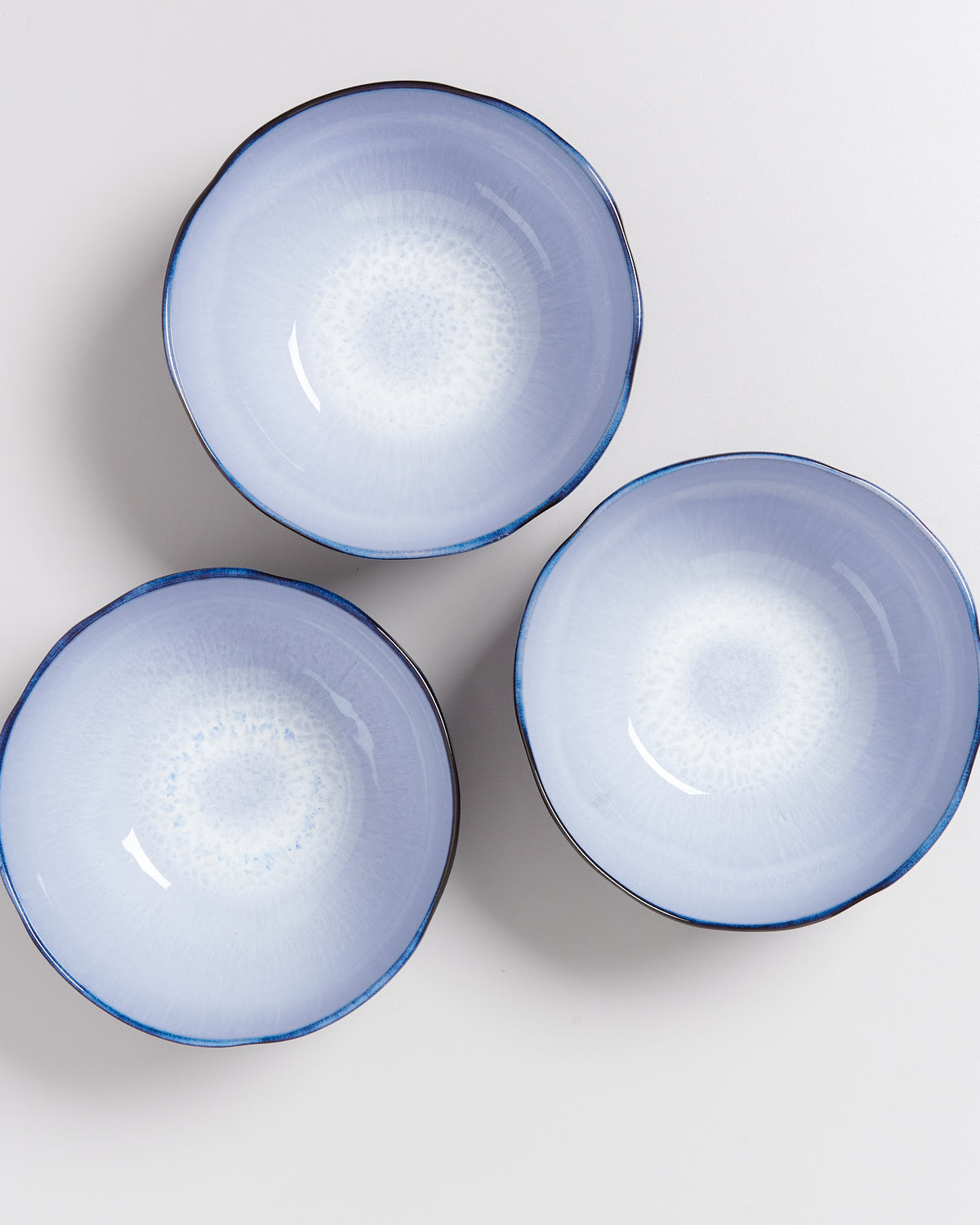 Drei blaue Keramikschalen mit mandalaähnlichen Mustern auf einer weißen Oberfläche arrangiert.