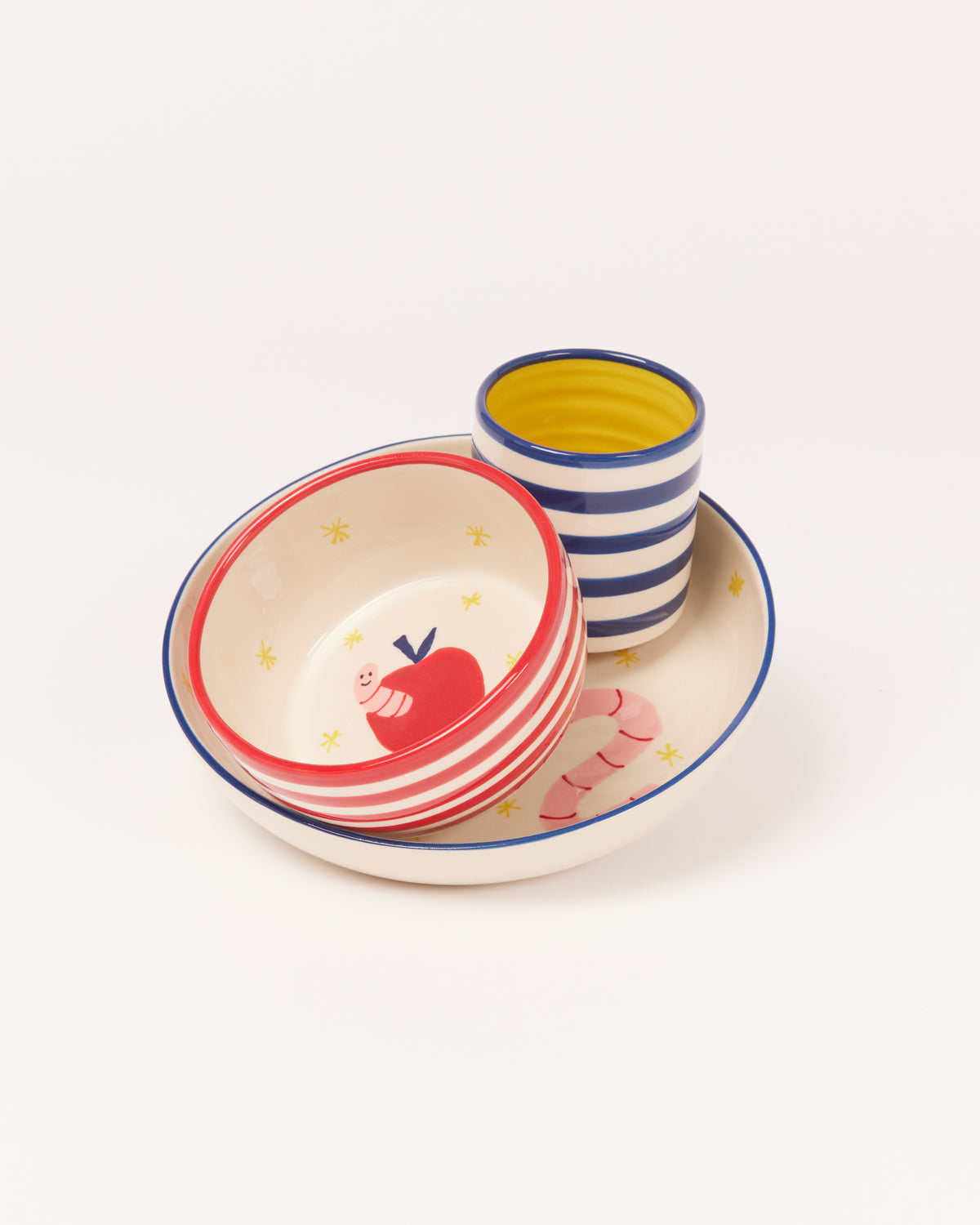 Set aus gestreiftem Geschirr mit Apfel- und Wurm-Motiv, bestehend aus Schüssel, Teller und Becher.