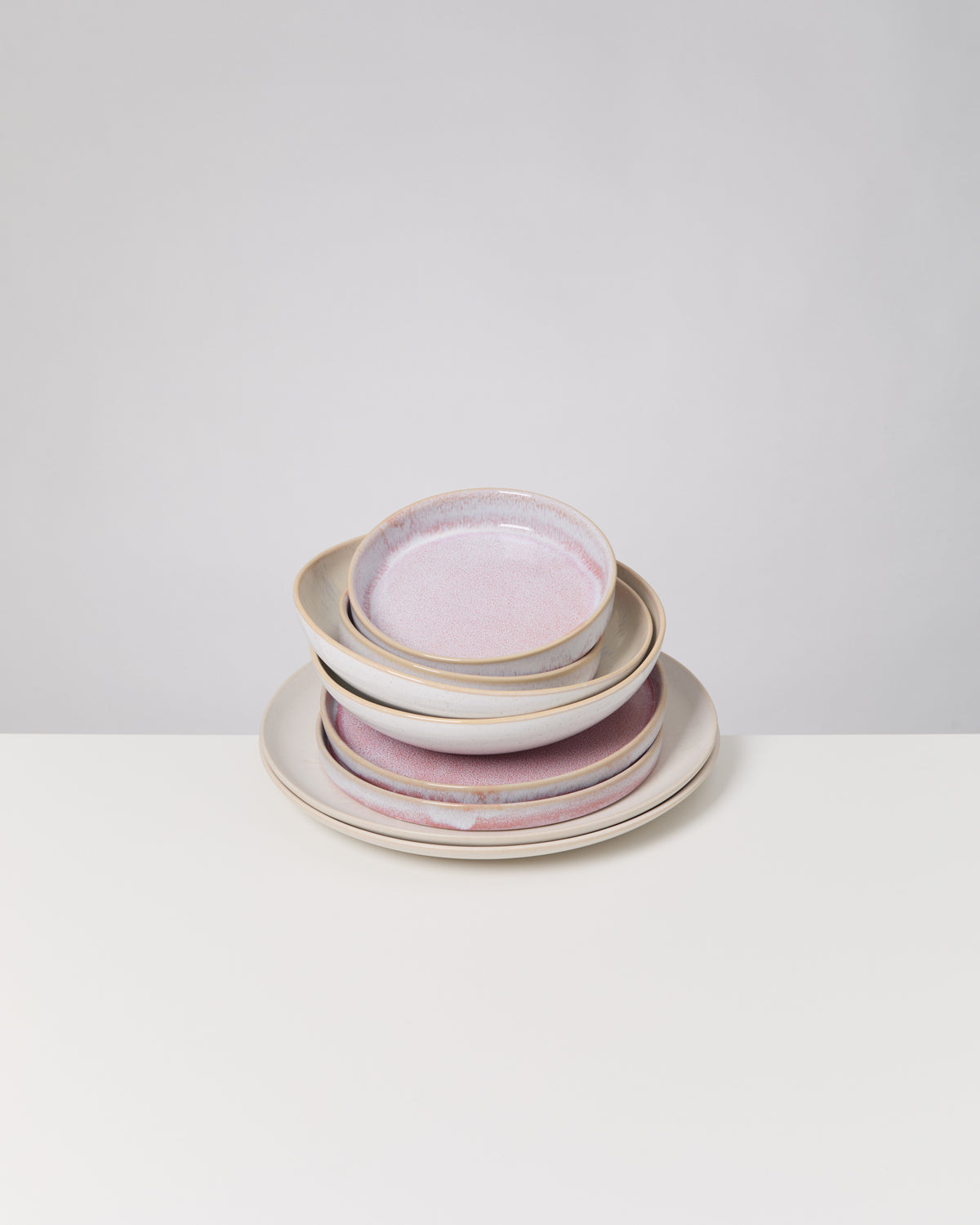 Ein Stapel Keramikteller und -schalen mit rosa Glasur steht auf einem weißen Tisch.