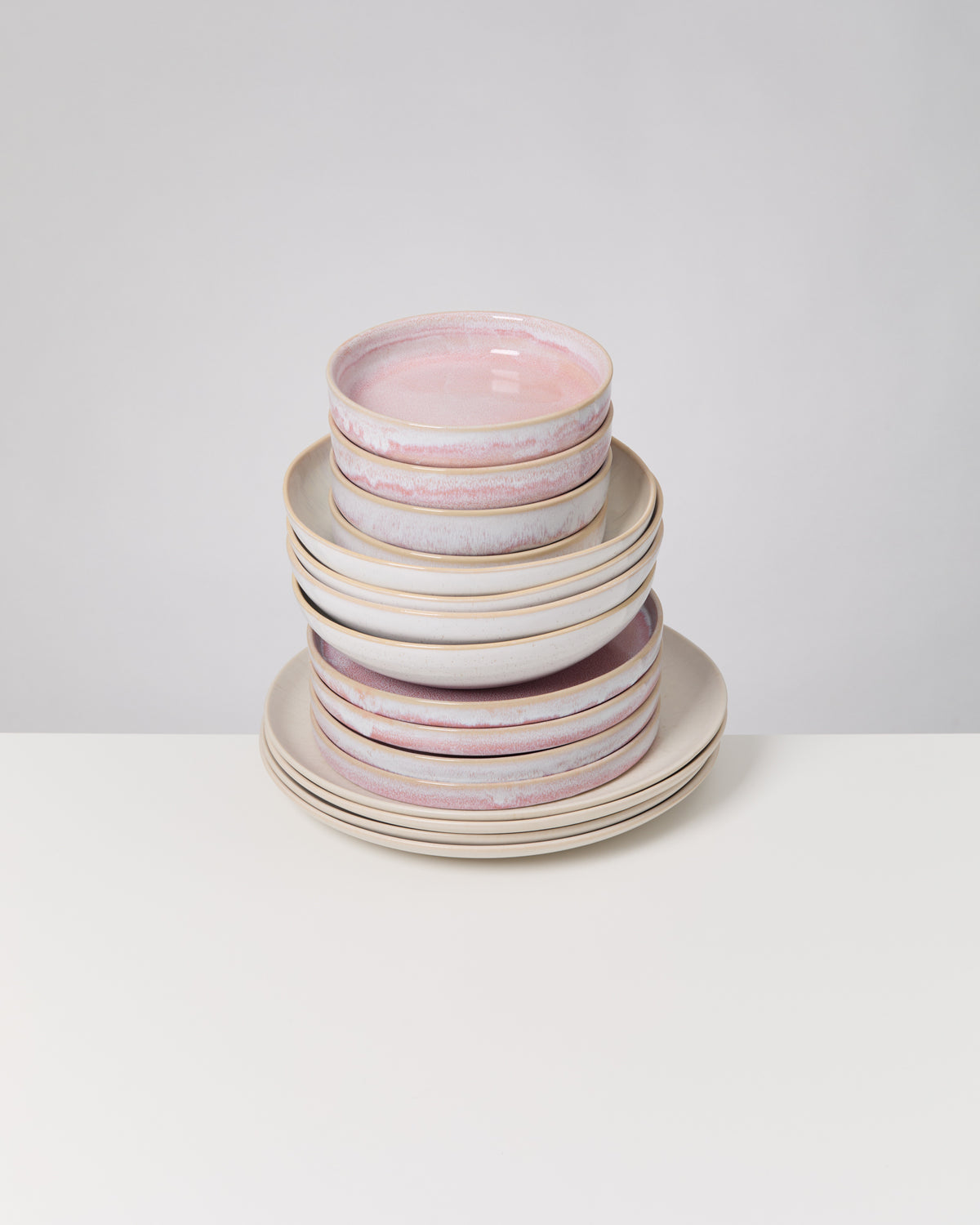 Ein Stapel von Keramikgeschirr mit rosa und weißen Tellern und Schalen auf einem weißen Tisch.