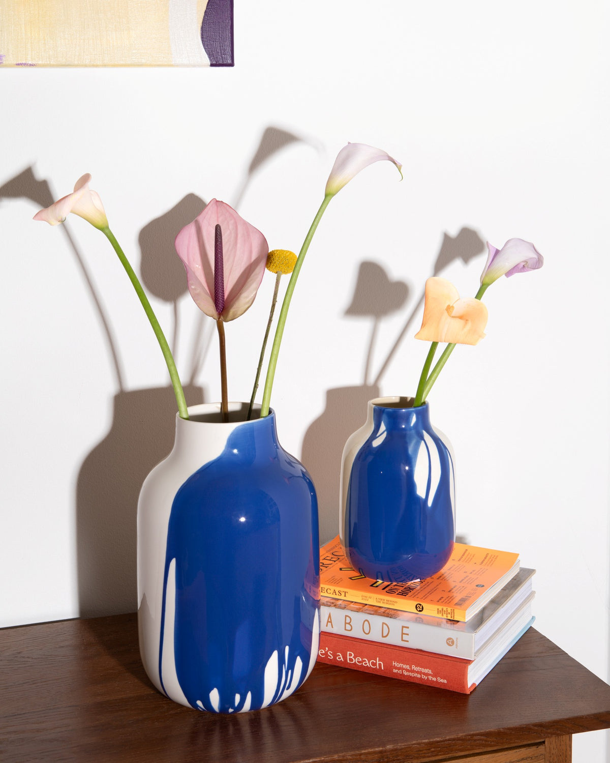 Zwei blaue Vasen mit Blumen stehen auf einem Holztisch, eine auf mehreren gestapelten Büchern.
