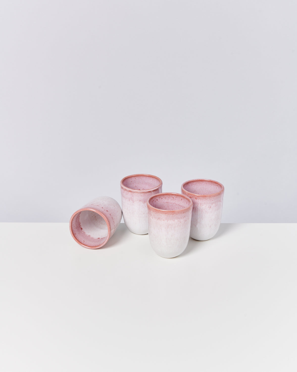 Vier weiße Keramikbecher mit rosa Rand auf weißem Hintergrund, einer liegt seitlich.