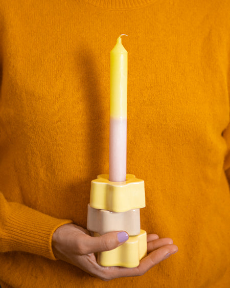 Person hält eine zweifarbige Kerze in einem gelben Kerzenhalter vor einem orangefarbenen Pullover.