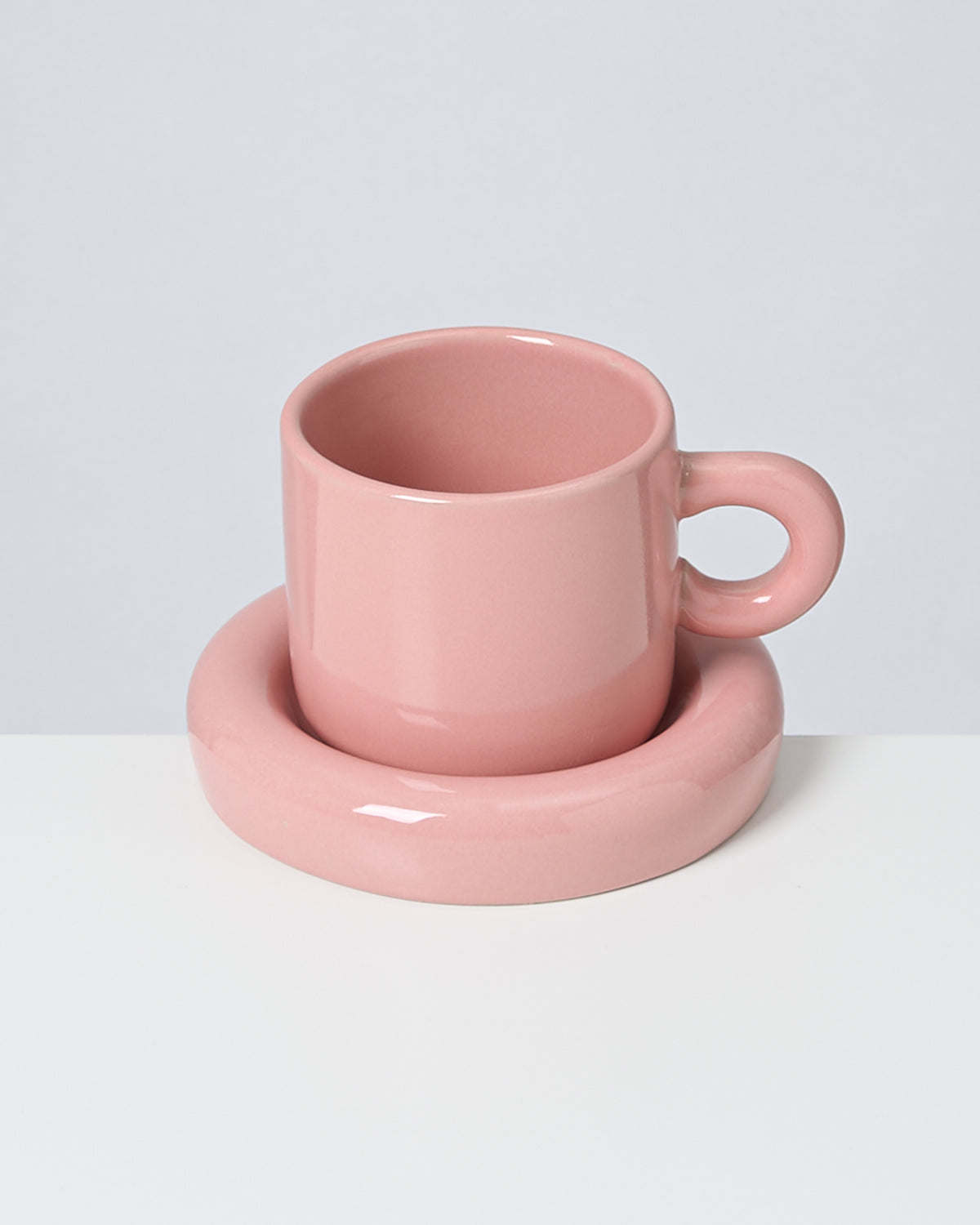 Rosa Tasse mit passender rosa Untertasse auf weißem Hintergrund.