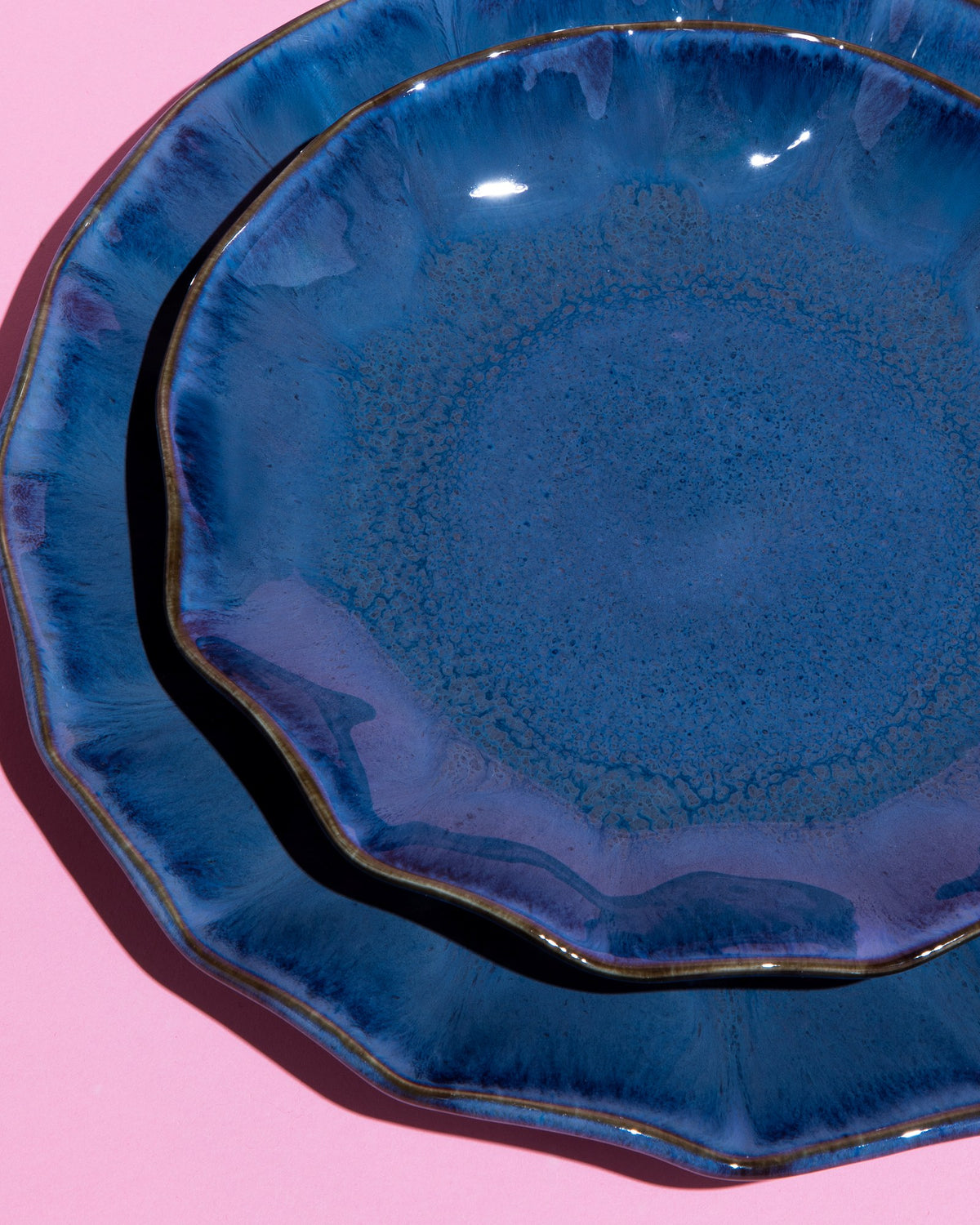 Zwei blaue Keramikteller mit unregelmäßigem Rand liegen übereinander auf einem rosa Hintergrund.