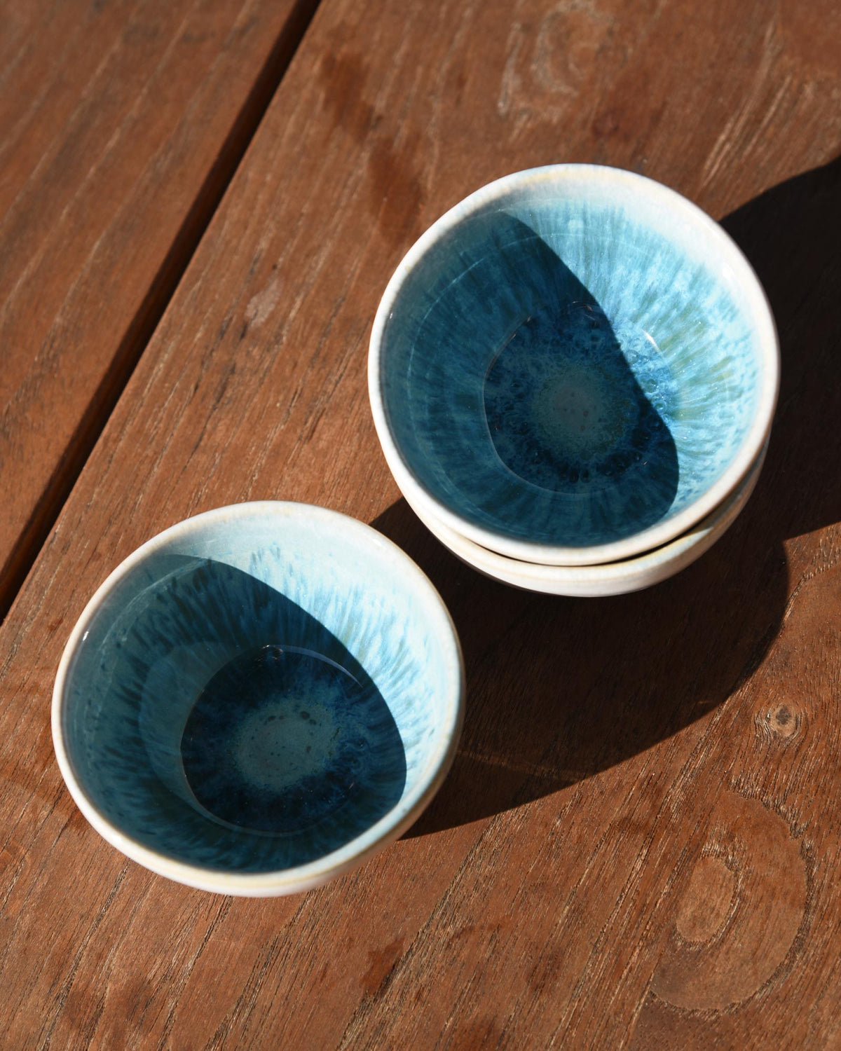 Keramische Schalen mit blauem Innenmuster stehen auf einem Holztisch in der Sonne.