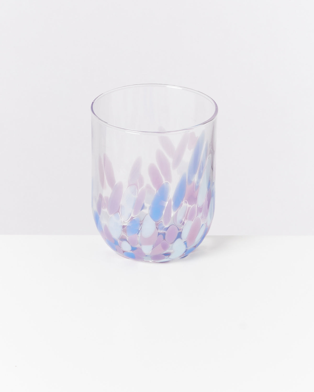 Ein gläserner Becher mit lila, rosa und blauen Mustern auf weißem Hintergrund.