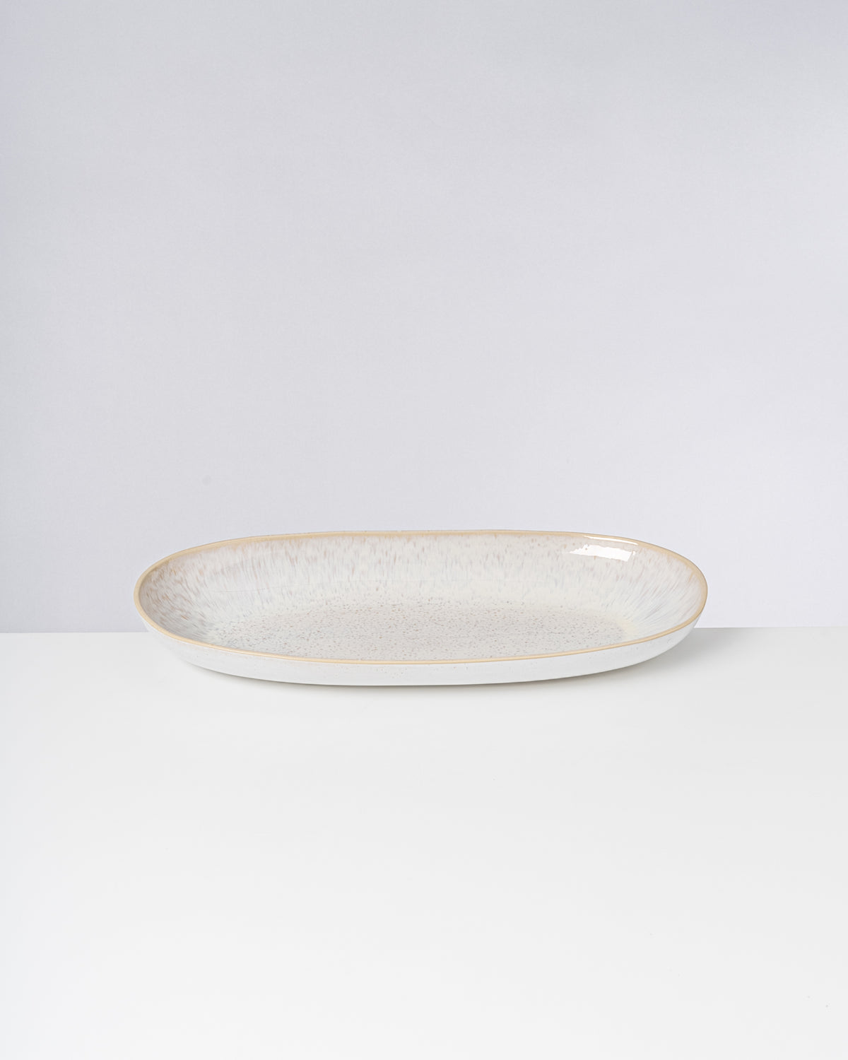 Ovaler, weißer Keramikteller mit leichtem Farbverlauf und minimalistischem Design auf weißem Hintergrund.