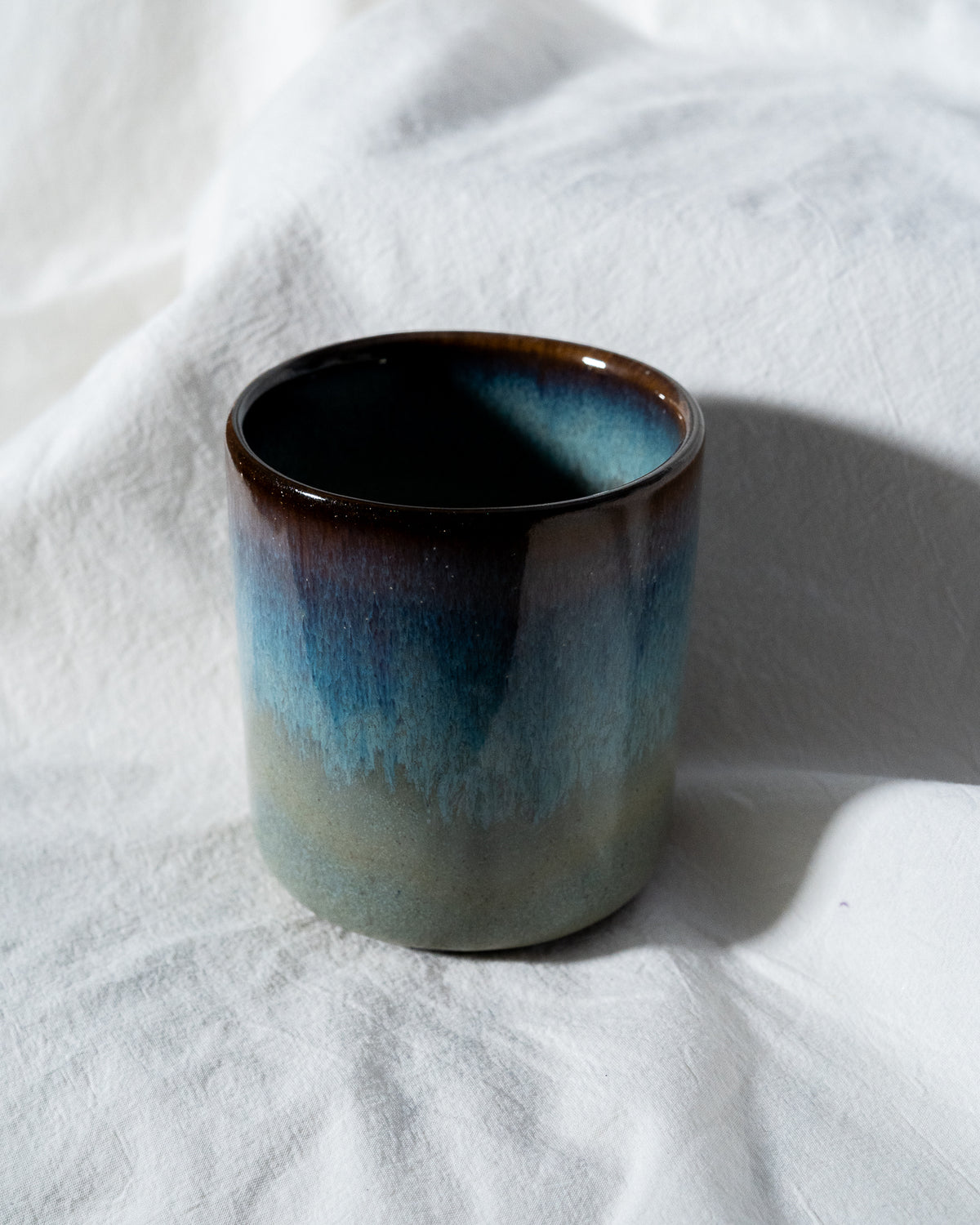 Eine Keramiktasse mit blau-braunem Farbverlauf steht auf einem weißen Tuch.