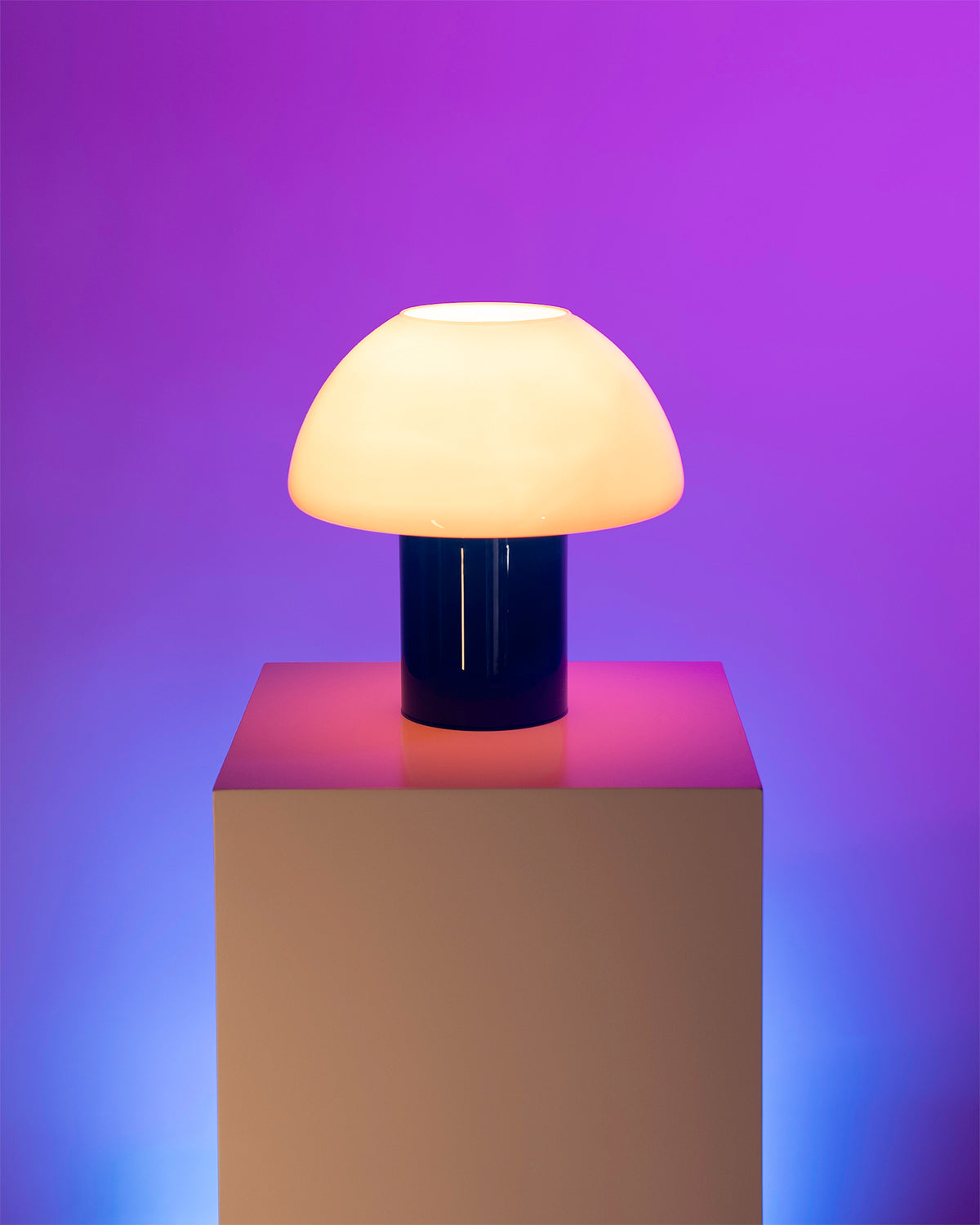 Stehlampe mit cremefarbenem Schirm und dunklem Sockel auf einem Podest vor einem lila-blauen Hintergrund.